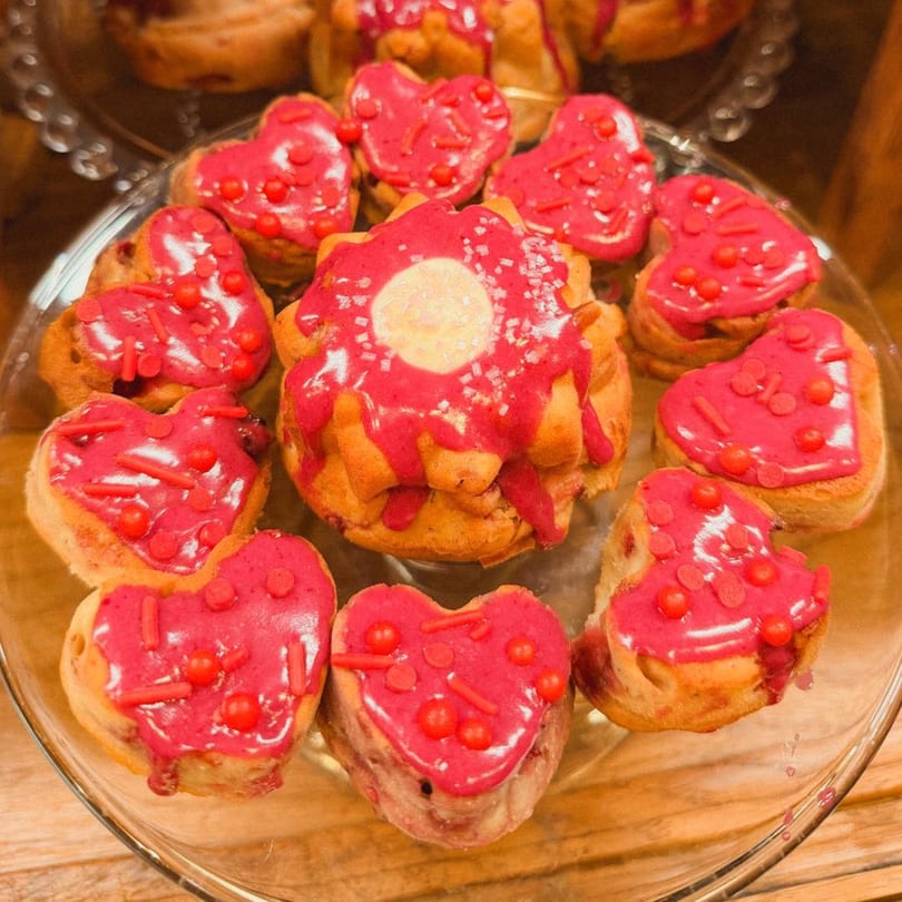 Heart-shaped and fluted cakes with pink icing and red sprinkles on a glass platter.