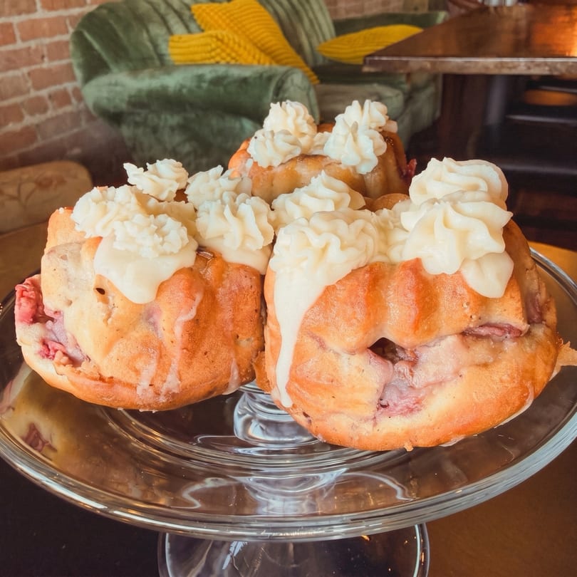 Bundt cakes with white frosting and whipped cream on a glass stand in a cozy setting.