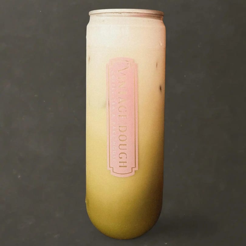 A tall, clear glass of iced matcha latte with a pink "Vintage Dough" label.