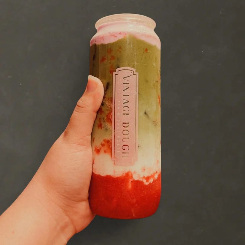 Hand holding a layered drink with red, white, and green sections, labeled "Vintage Dough".