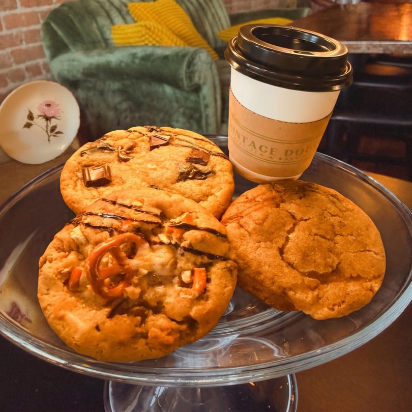 Three cookies and a Vintage Doughnuts coffee cup on a glass stand, with a green couch in the background.